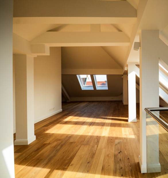 Photograph of sunlit modern loft conversion with wooden flooring.